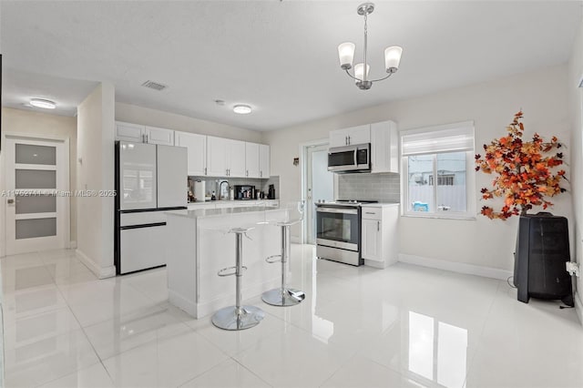 kitchen featuring visible vents, white cabinets, stainless steel appliances, light countertops, and backsplash