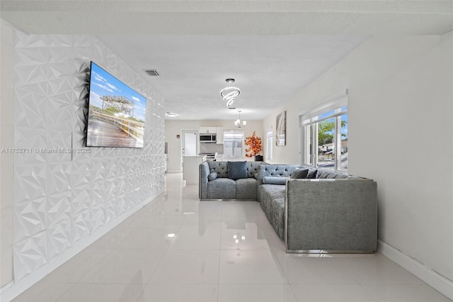 living room featuring a chandelier, a textured ceiling, light tile patterned flooring, visible vents, and baseboards