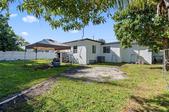 back of property featuring central AC unit, a fenced backyard, a yard, a carport, and stucco siding