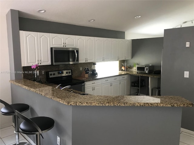 16654 SW 103rd Ln, Miami, FL 33196 - kitchen with decorative backsplash, appliances with stainless steel finishes, white cabinetry, light tile patterned flooring, and a peninsula