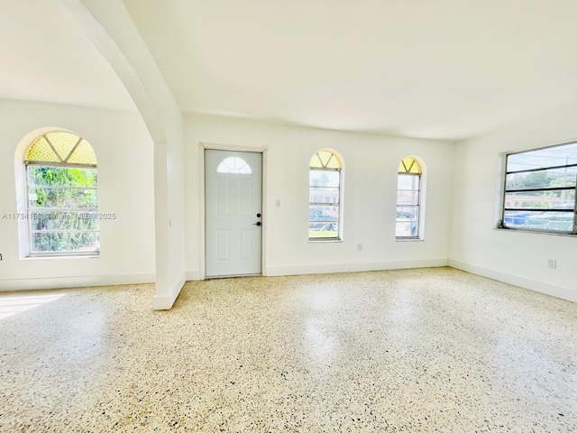 foyer featuring arched walkways, speckled floor, and baseboards