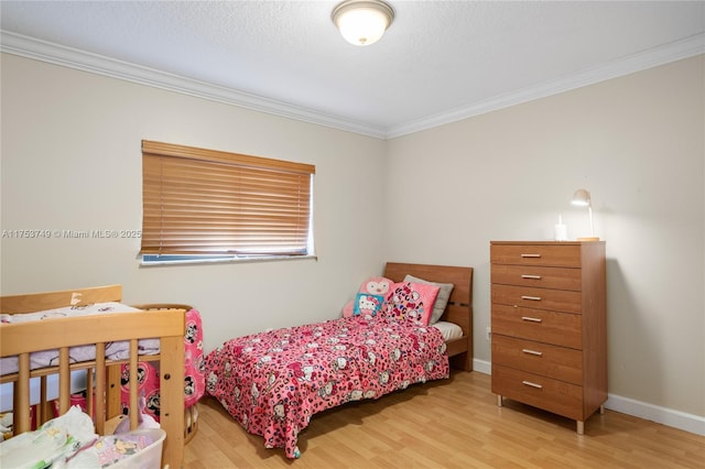 bedroom with a textured ceiling, ornamental molding, light wood-style flooring, and baseboards