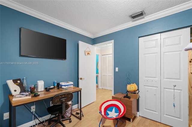 office with light wood-style flooring, visible vents, a textured ceiling, and ornamental molding