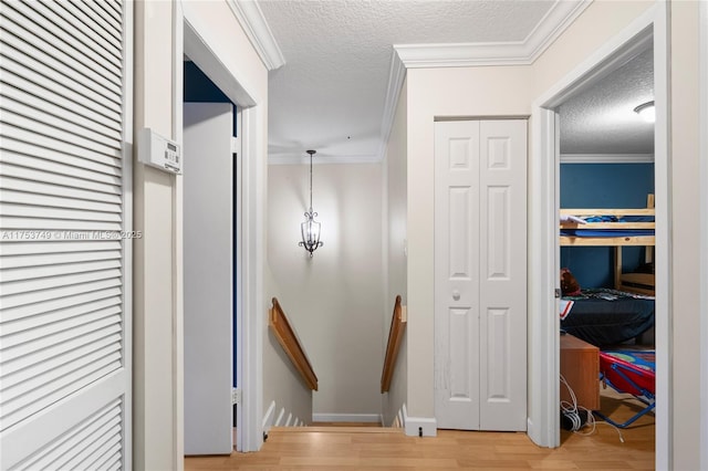 hall with light wood-type flooring, ornamental molding, a textured ceiling, and an upstairs landing