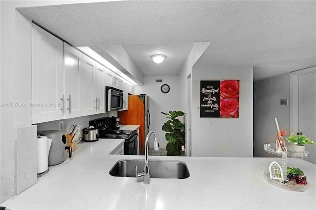 kitchen with white cabinets, stainless steel appliances, a textured ceiling, light countertops, and a sink