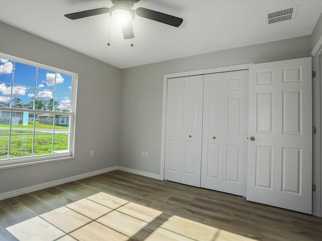 unfurnished bedroom featuring a closet, visible vents, baseboards, and wood finished floors