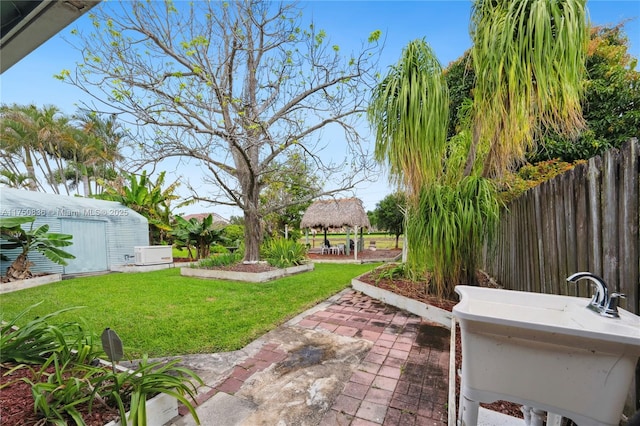 view of yard featuring a patio, an outdoor structure, a sink, fence, and a gazebo