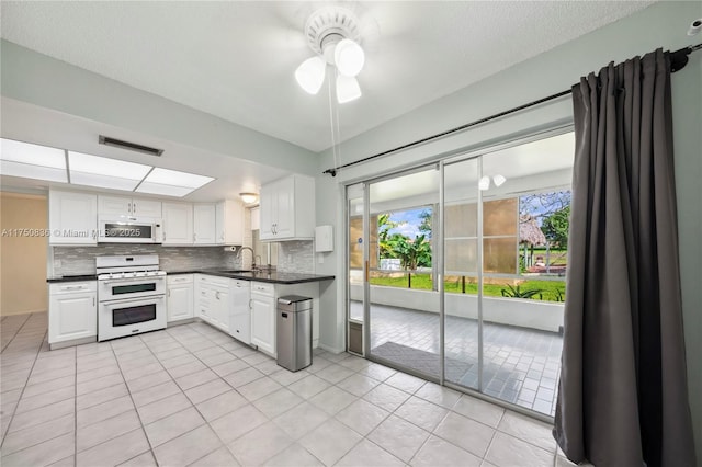 kitchen with dark countertops, white appliances, white cabinetry, and decorative backsplash