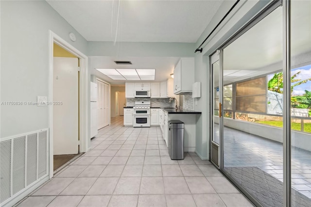 kitchen featuring white appliances, tasteful backsplash, visible vents, dark countertops, and white cabinetry