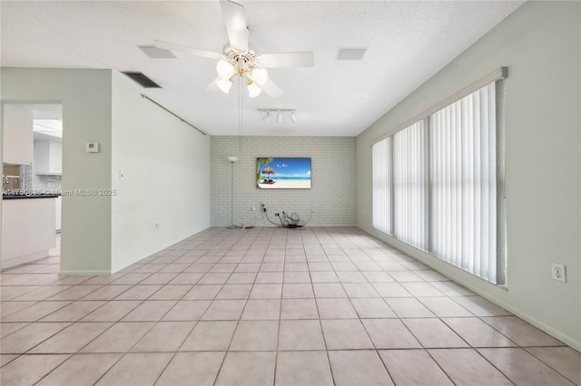 spare room with light tile patterned floors, visible vents, brick wall, ceiling fan, and a textured ceiling