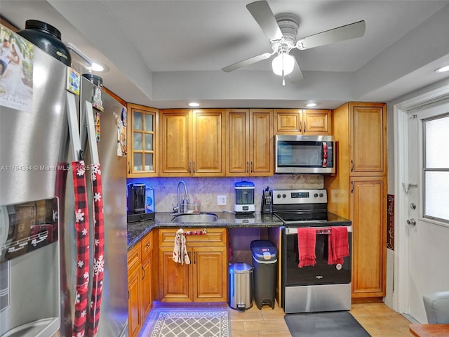 kitchen with dark stone counters, stainless steel appliances, brown cabinetry, and a sink