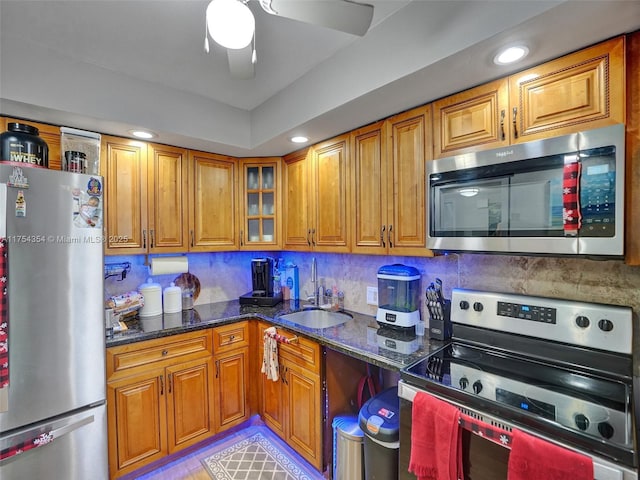 kitchen featuring a sink, appliances with stainless steel finishes, brown cabinets, dark stone countertops, and glass insert cabinets