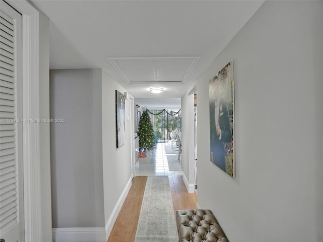 corridor featuring light wood-type flooring, attic access, and baseboards