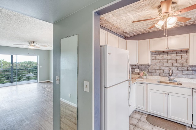 kitchen with tasteful backsplash, light countertops, freestanding refrigerator, white cabinetry, and a sink