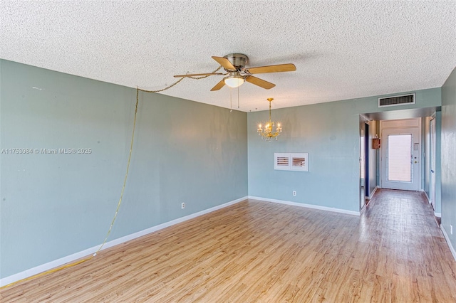 empty room featuring baseboards, visible vents, wood finished floors, a textured ceiling, and ceiling fan with notable chandelier