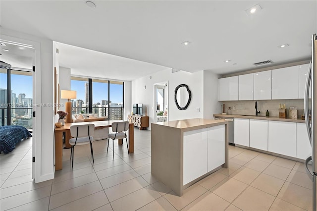 kitchen featuring visible vents, a sink, a view of city, white cabinetry, and backsplash