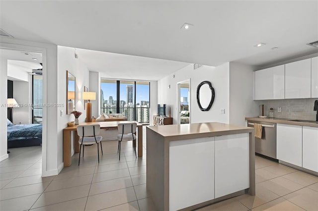 kitchen with light tile patterned floors, decorative backsplash, stainless steel dishwasher, white cabinetry, and a kitchen island