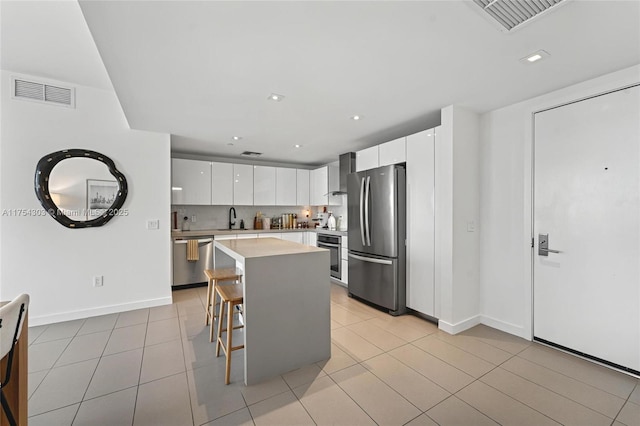 kitchen with stainless steel appliances, wall chimney exhaust hood, a sink, and visible vents