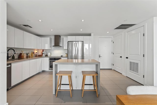 kitchen with light tile patterned floors, appliances with stainless steel finishes, wall chimney range hood, and visible vents