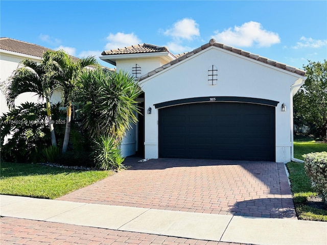 mediterranean / spanish-style house featuring a garage, a tiled roof, decorative driveway, and stucco siding