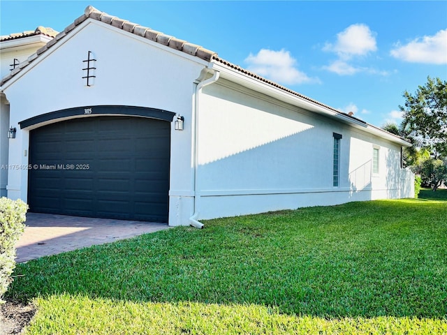 view of side of property with stucco siding, a lawn, an attached garage, driveway, and a tiled roof