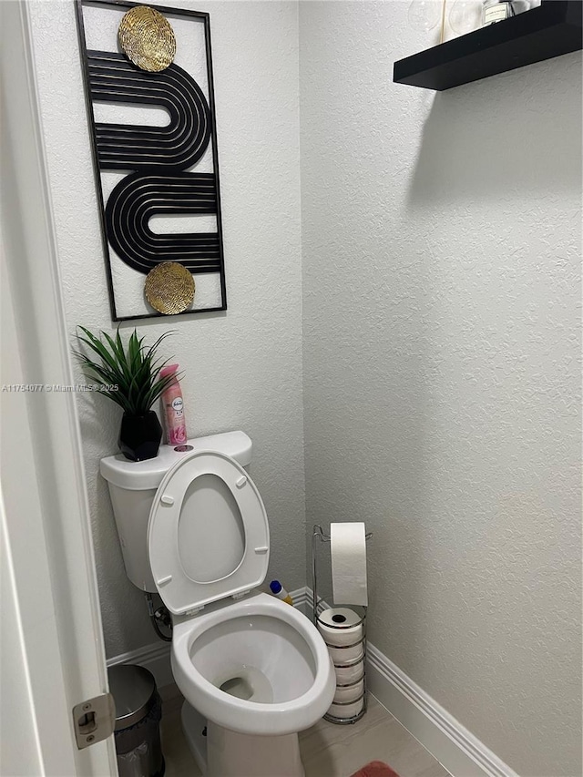 bathroom with a textured wall, toilet, and baseboards