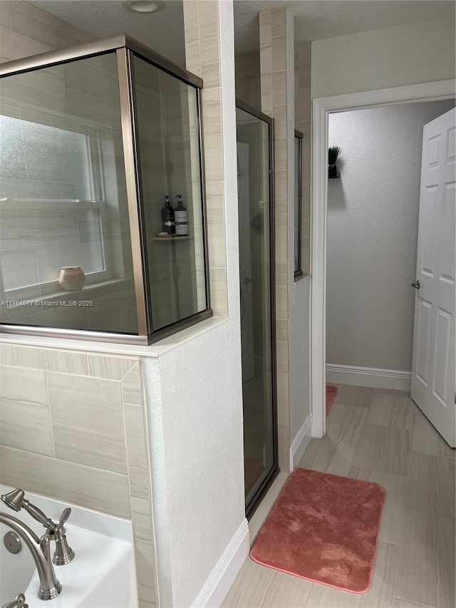 bathroom featuring a textured wall, a stall shower, a bath, and baseboards