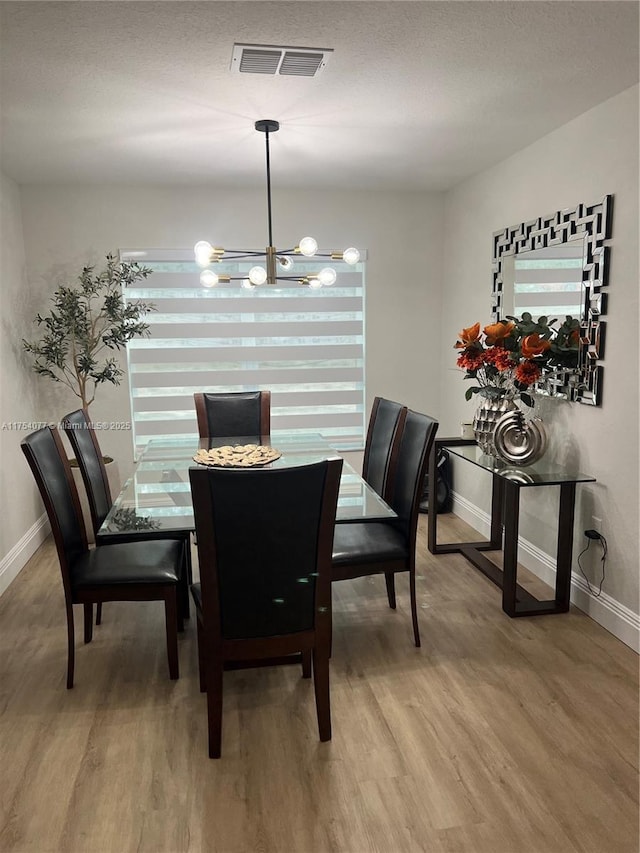 dining room featuring baseboards, light wood-type flooring, visible vents, and an inviting chandelier