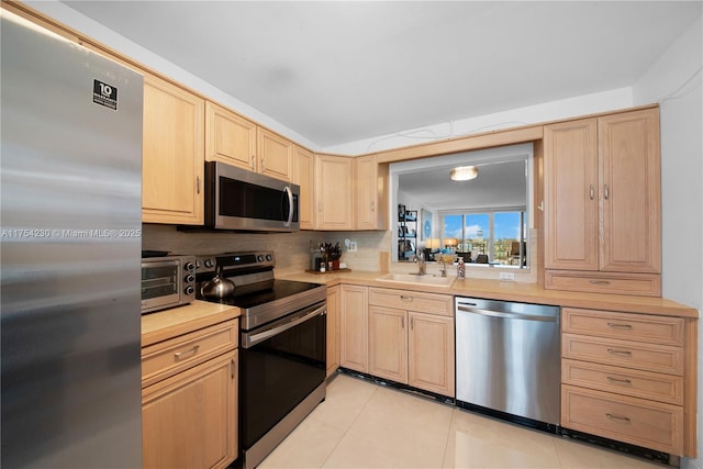 kitchen featuring a toaster, light countertops, stainless steel appliances, light brown cabinetry, and a sink