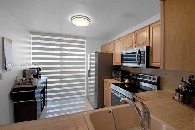 kitchen featuring a toaster, light countertops, light brown cabinetry, appliances with stainless steel finishes, and a sink