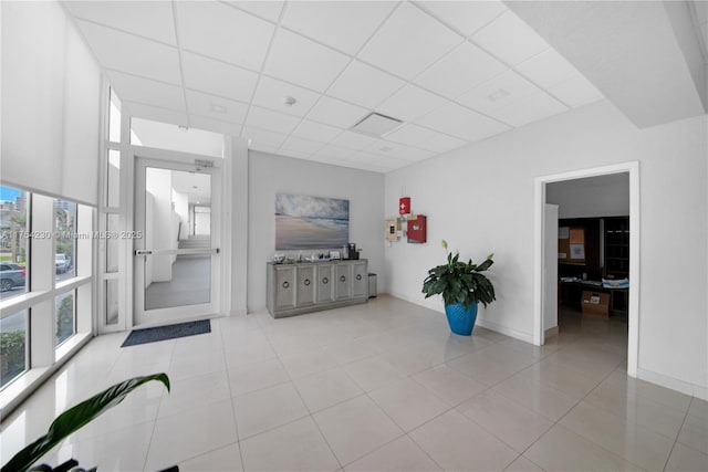 unfurnished living room with tile patterned flooring, a paneled ceiling, and baseboards