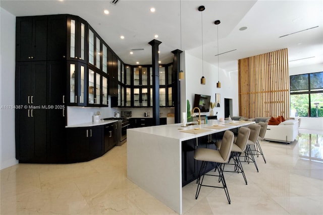 kitchen with stainless steel stove, glass insert cabinets, dark cabinets, a large island with sink, and a kitchen breakfast bar