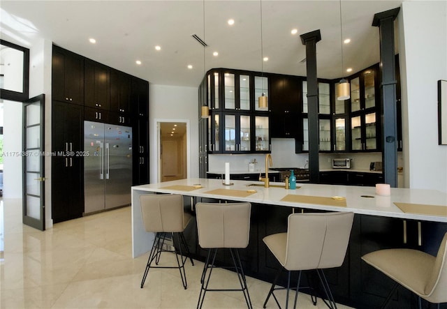 kitchen featuring built in fridge, a breakfast bar, light countertops, glass insert cabinets, and a sink