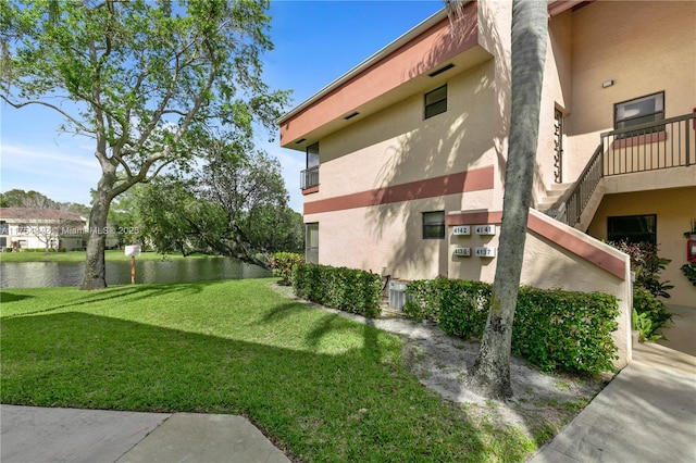 view of side of property featuring a lawn, a water view, and stucco siding