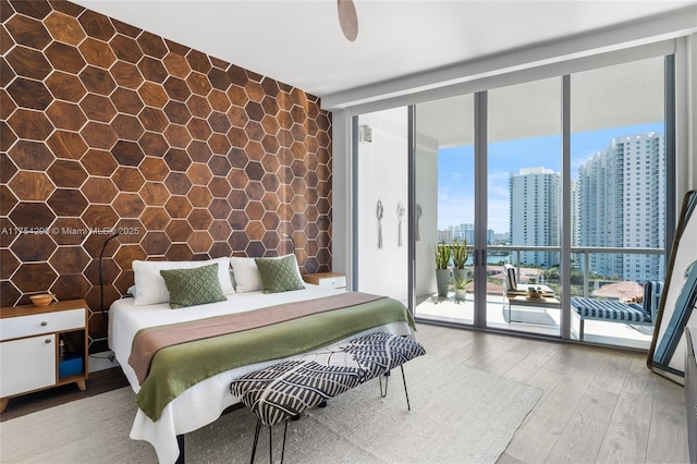 bedroom with access to exterior, a view of city, floor to ceiling windows, a ceiling fan, and wood finished floors