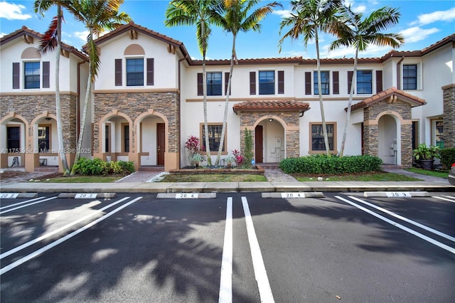 view of front of home featuring stone siding, a tile roof, uncovered parking, and stucco siding