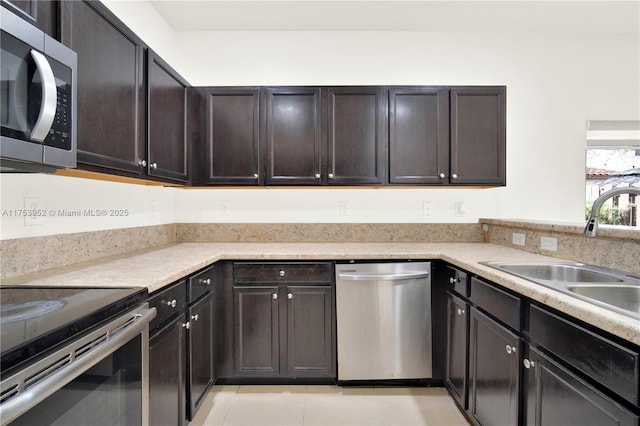 kitchen with light tile patterned floors, stainless steel appliances, a sink, dark brown cabinets, and light stone countertops