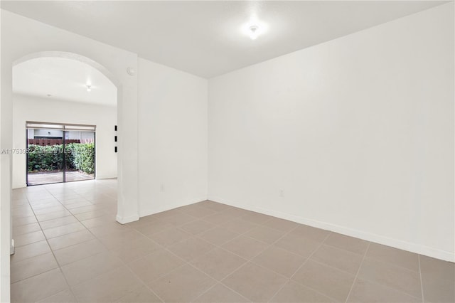 unfurnished room featuring baseboards, arched walkways, and tile patterned floors