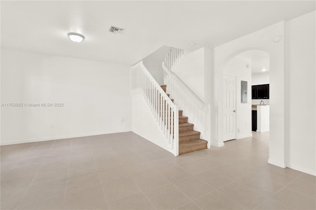 tiled spare room with arched walkways, visible vents, baseboards, and stairs