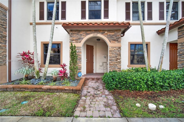 property entrance featuring stone siding, a tiled roof, and stucco siding