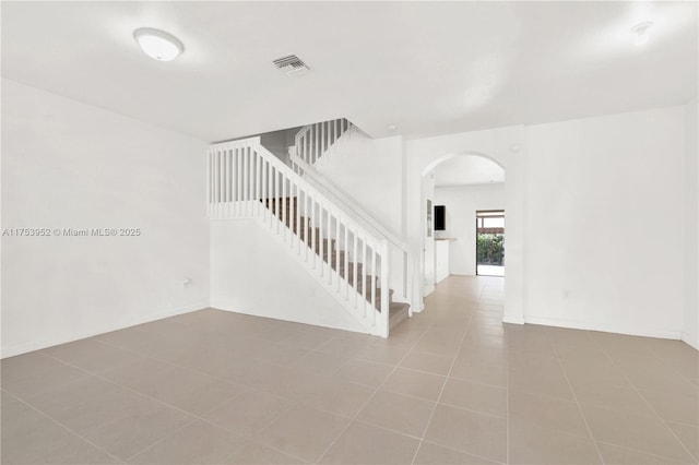 stairway with arched walkways, tile patterned floors, visible vents, and baseboards