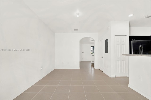 empty room featuring arched walkways, visible vents, tile patterned flooring, electric panel, and baseboards