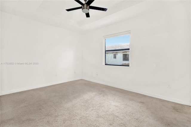 carpeted spare room featuring a ceiling fan, baseboards, and a tray ceiling