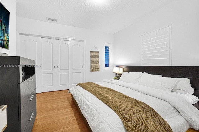 bedroom with light wood finished floors, a textured ceiling, visible vents, and a closet