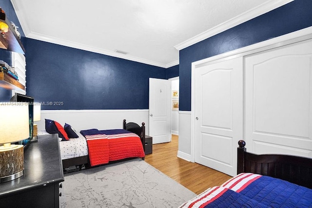 bedroom featuring a wainscoted wall, wood finished floors, visible vents, ornamental molding, and a closet