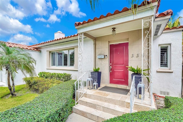 doorway to property with a tiled roof, crawl space, a chimney, and stucco siding