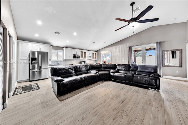 living room featuring a wealth of natural light, visible vents, vaulted ceiling, and light wood finished floors