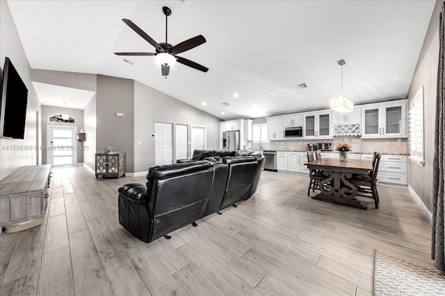 living room with light wood-type flooring, baseboards, high vaulted ceiling, and a ceiling fan