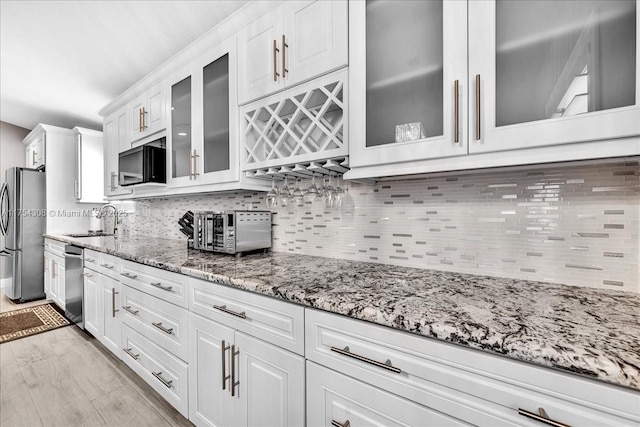 kitchen with tasteful backsplash, appliances with stainless steel finishes, light stone counters, white cabinetry, and a sink