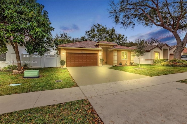 mediterranean / spanish house with an attached garage, a tile roof, concrete driveway, a yard, and stucco siding